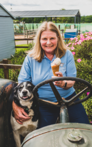 Older woman wearing bright blue jacket holding an ice cream in left hand and smiling to the camera whilst with right hand holding black and white border collie dog that is also smiling to the camera - Proud Finalist at the 2024 East Midlands Chamber Business Awards