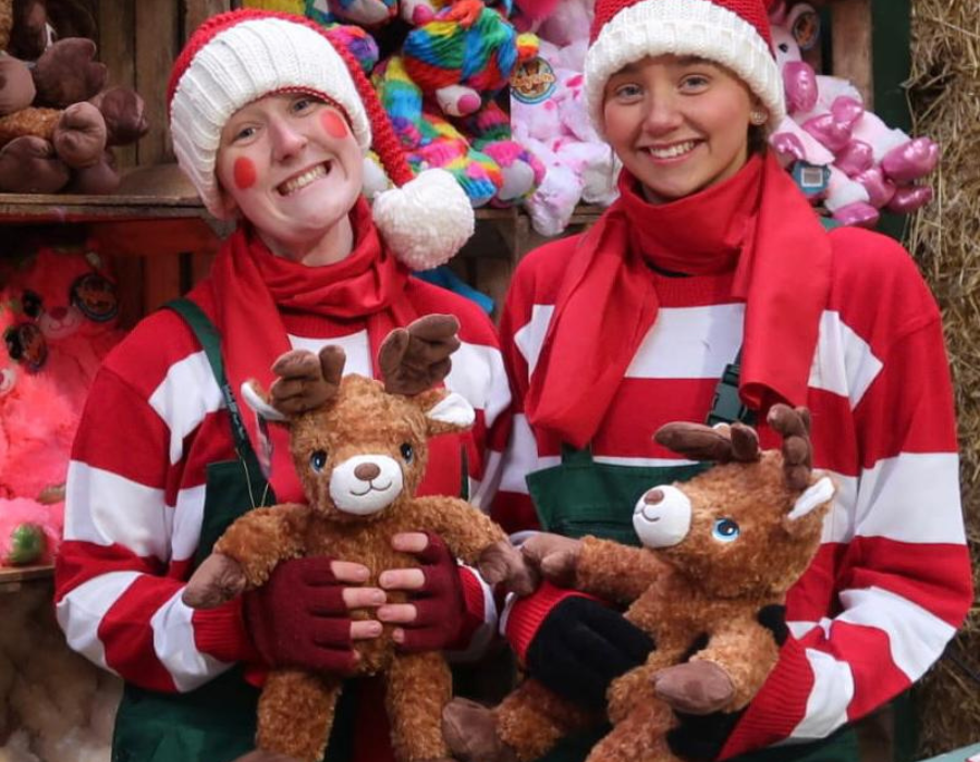 two women dressed as elves in white, red and green costumer holding reindeer teddy bears during the best Christmas event in Derby